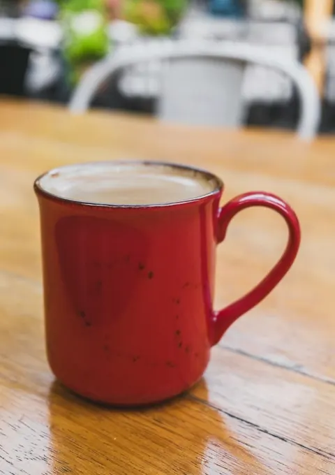 Phone photo of a red mug of coffee on a wooden table
